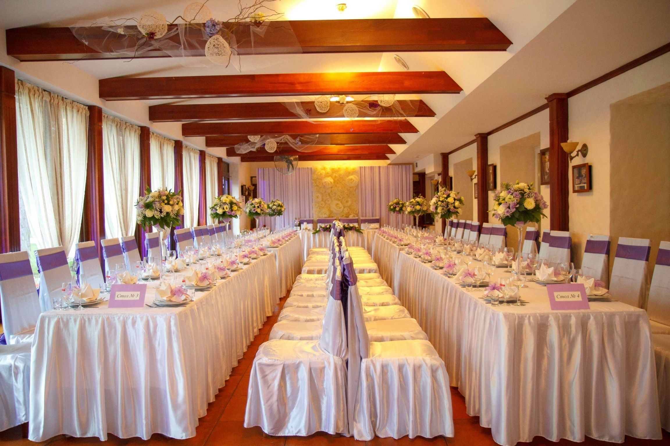 A long banquet table with white tablecloths and purple sashes, set for a formal event.