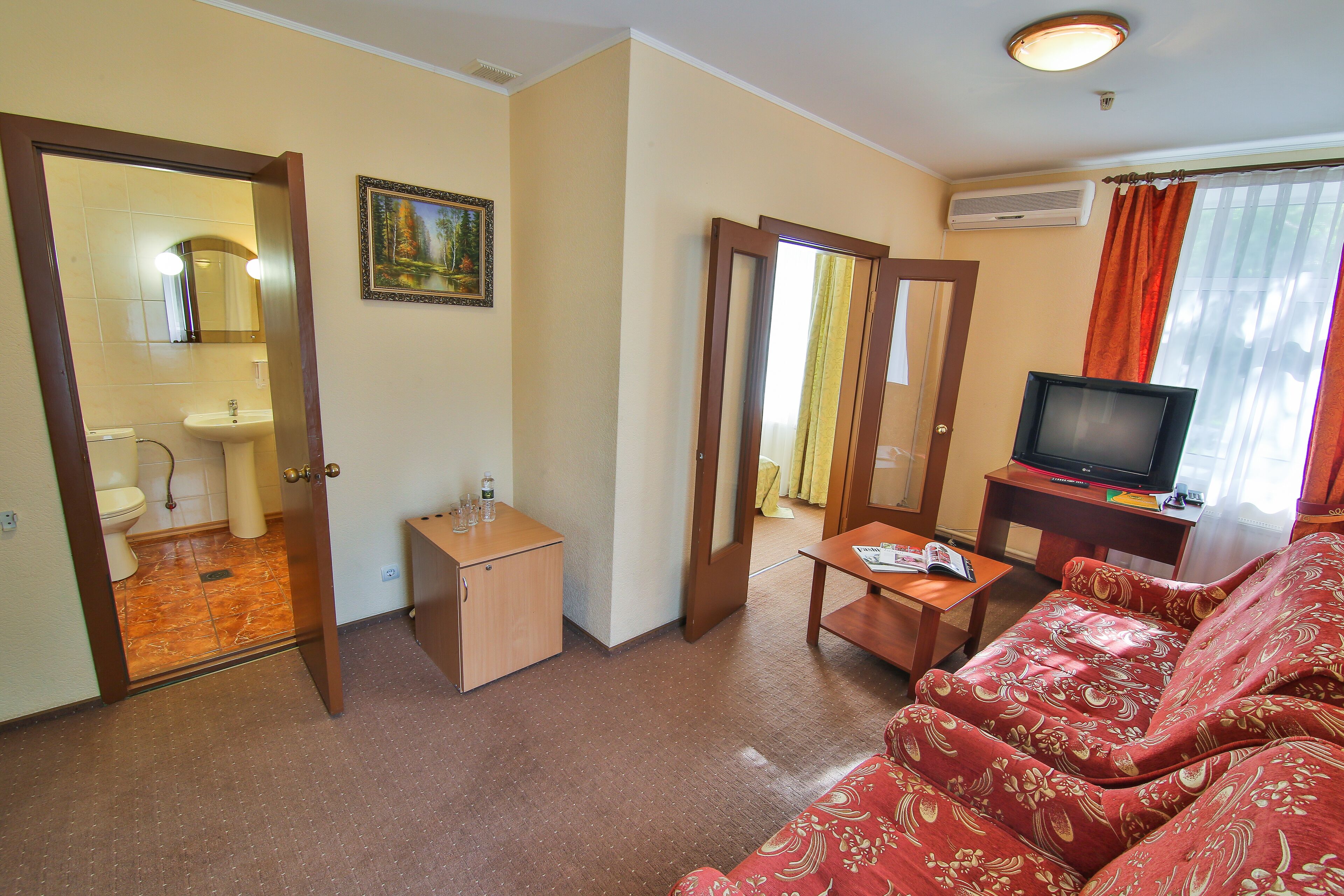 A living room with a sofa, a television, a small table, and a door leading to a bathroom.