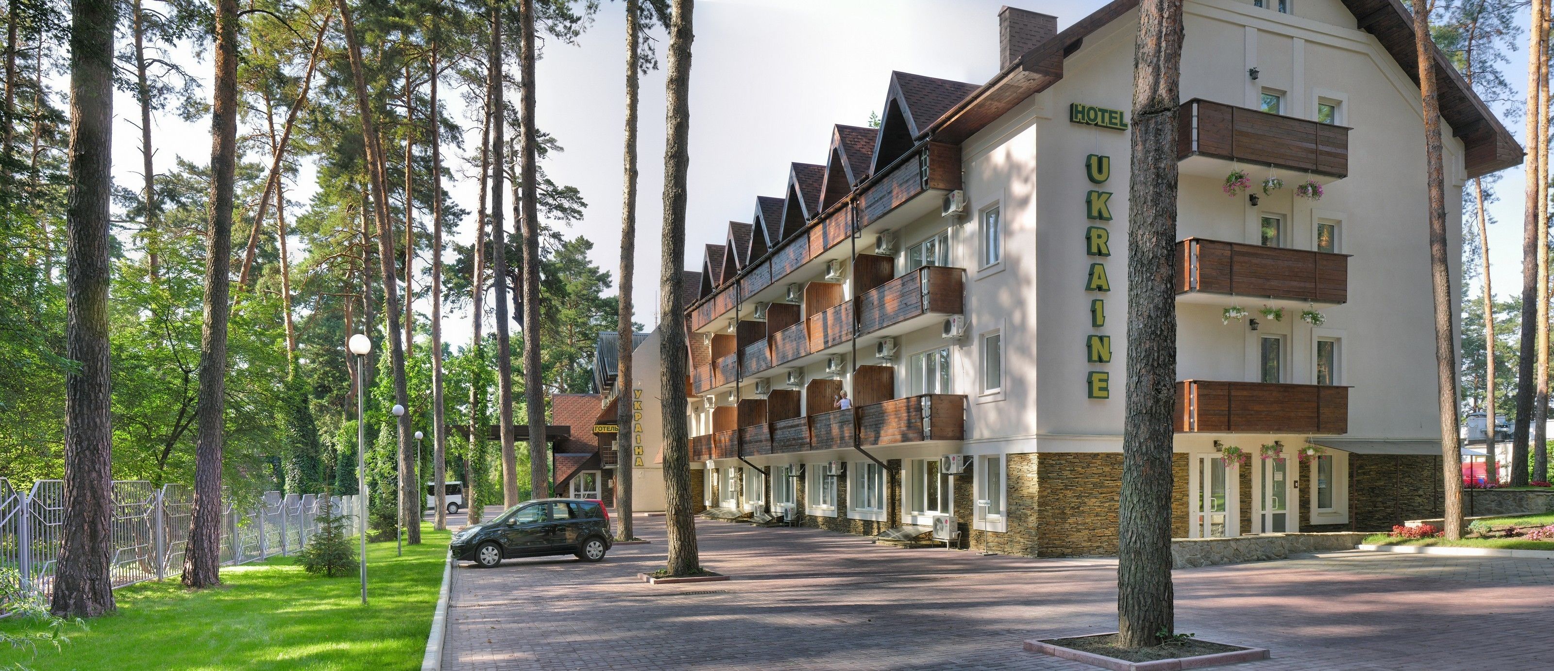 A hotel with multiple balconies, a paved driveway, and a surrounding forested area.