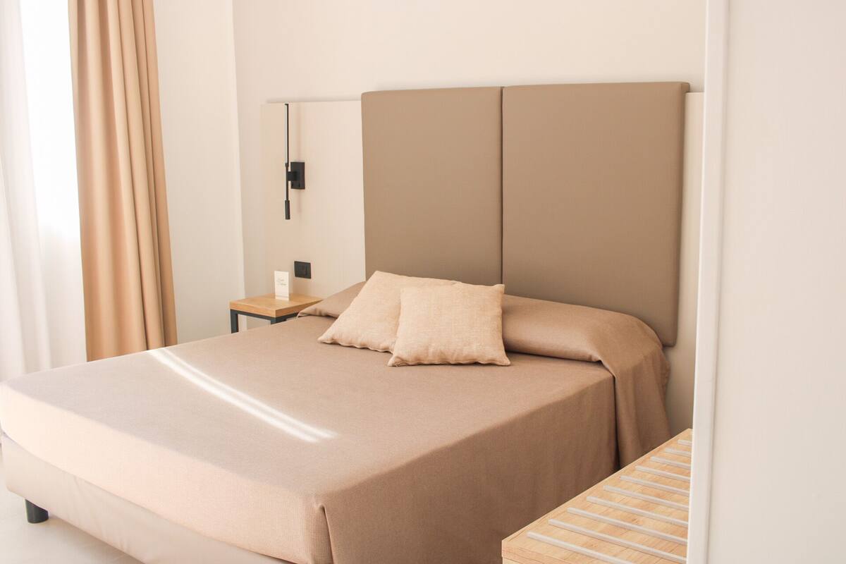 Una habitación de hotel con cama, mesita de noche, lámpara y una mesita auxiliar de madera.