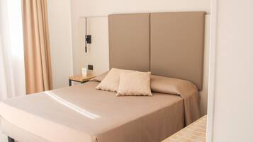 Een hotelkamer met een bed, nachtkastje, lamp en een houten bijzettafeltje.