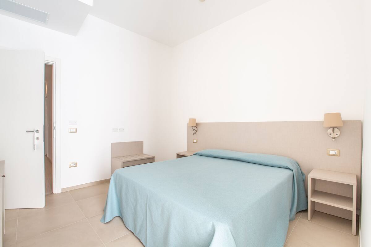 Un dormitorio con cama, mesitas de noche y un tocador.