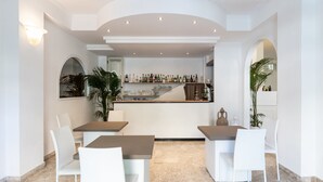 A modern bar area with a marble floor, white bar stools, and a variety of bottles and glasses on the shelves. - Hotel Falcone (Vieste)