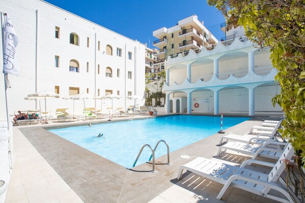 Piscina com espreguiçadeiras, posto de salva-vidas e uma bandeira.