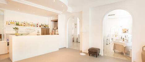A spacious hotel lobby with a reception desk, a bar area with various bottles, and a seating area with a bench.