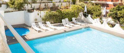 A rooftop pool with white lounge chairs and a view of the sea and buildings.