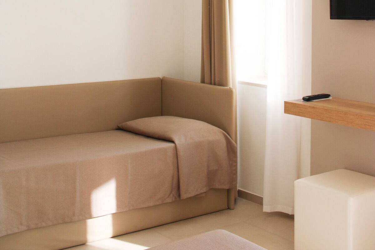 Una habitación moderna y minimalista con un sofá color beige, una mesita blanca y un televisor montado.