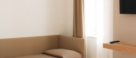 Una habitación moderna y minimalista con un sofá color beige, una mesita blanca y un televisor montado.