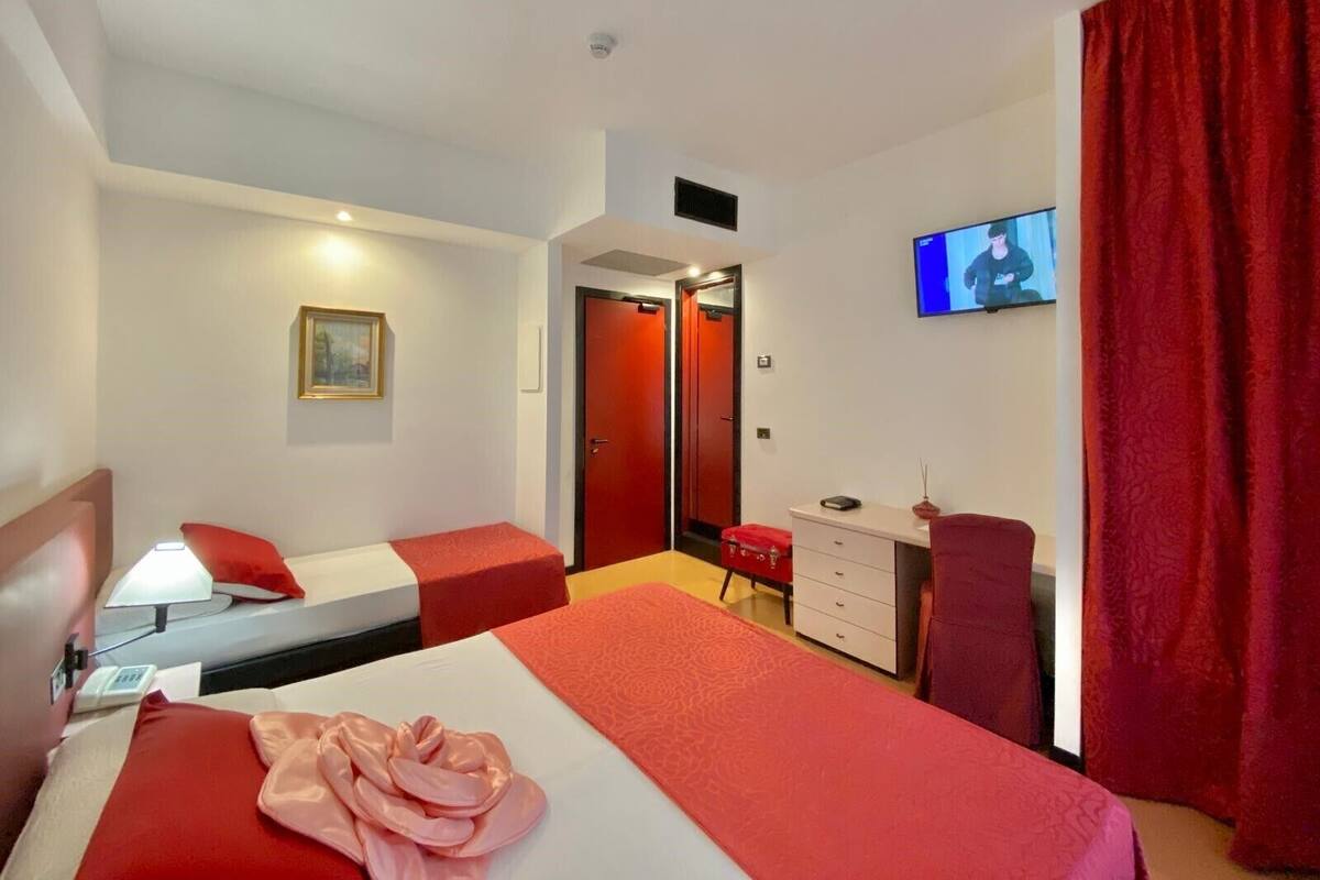 A hotel room with two beds, a desk, a chair, a TV, and a red curtain.