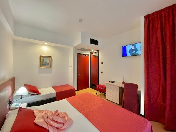 A hotel room with two beds, a desk, a chair, a TV, and a red curtain.
