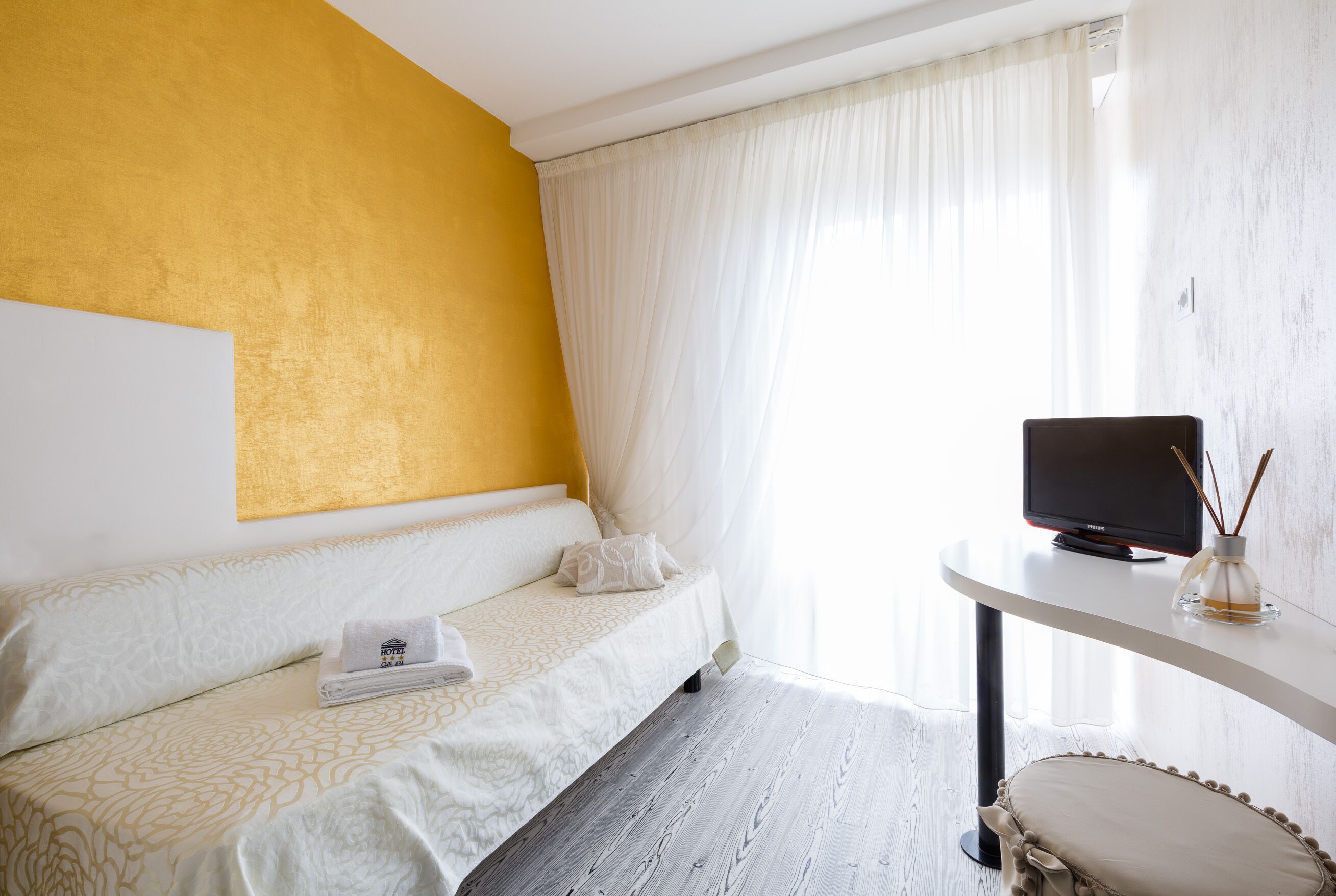 A hotel room with a bed, a television on a side table, and a window with curtains.