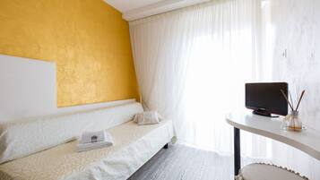 A hotel room with a bed, a television on a side table, and a window with curtains.