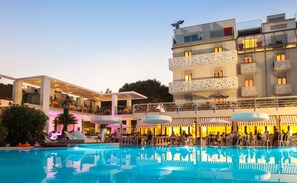 Un hotel con piscina, zona de estar exterior y espacio cubierto con mesas y sillas.