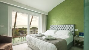A bedroom with a large bed, a chair, a nightstand, and a view through a sliding door to an outdoor area. - Hotel Ca' Di Valle (Cavallino-Treporti)