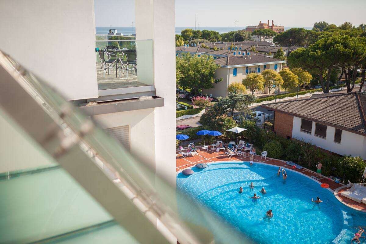 A pool area with lounge chairs and umbrellas, surrounded by residential buildings and greenery.
