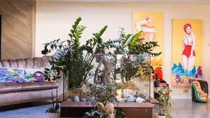 A living room with a sofa, a glass-top coffee table, and various plants. There are paintings on the wall and luggage in the background. - Hotel Ca' Di Valle (Cavallino-Treporti)