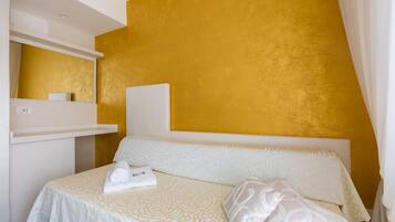 A hotel room with a bed, a white headboard, a mirror, and a shelf with a towel.