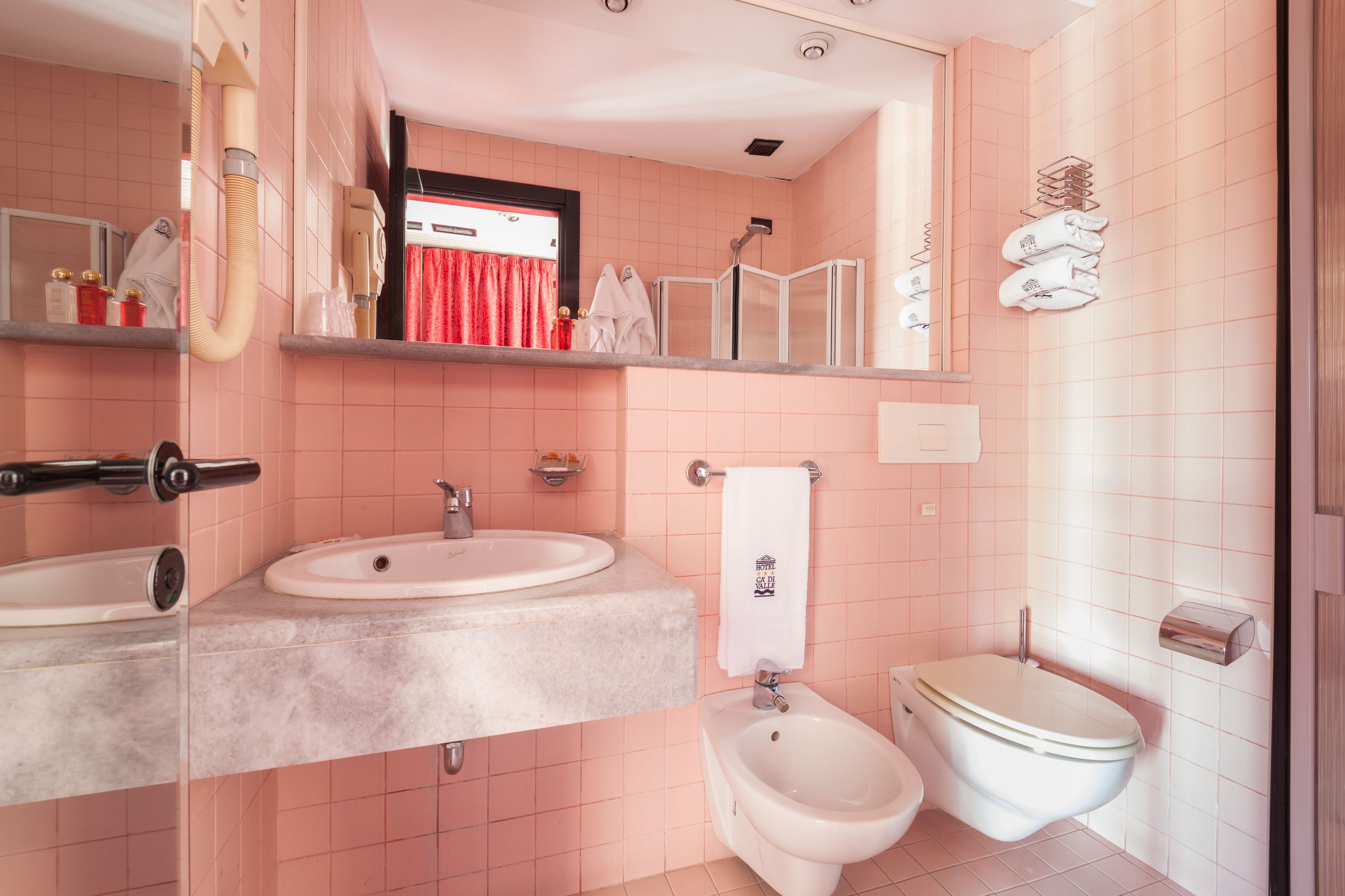 A bathroom with a sink, bidet, and toilet. There is a mirror above the sink and a towel rack.