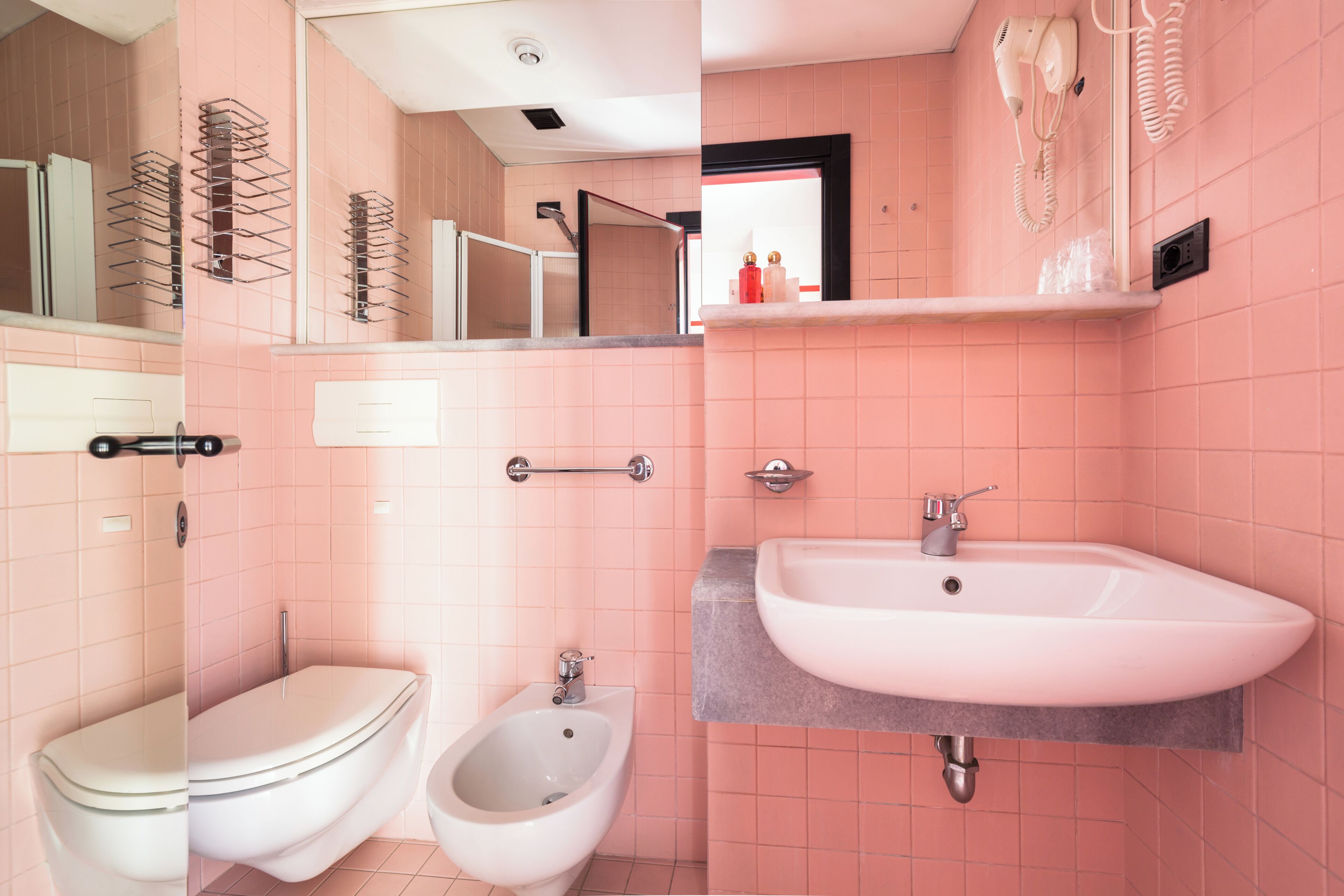 A bathroom with a toilet, bidet, and sink, pink tiled walls, and a mirror.