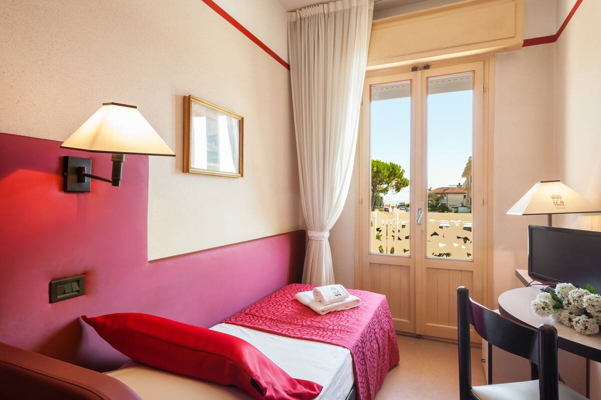 A hotel room with a bed, a desk, and a window with curtains.