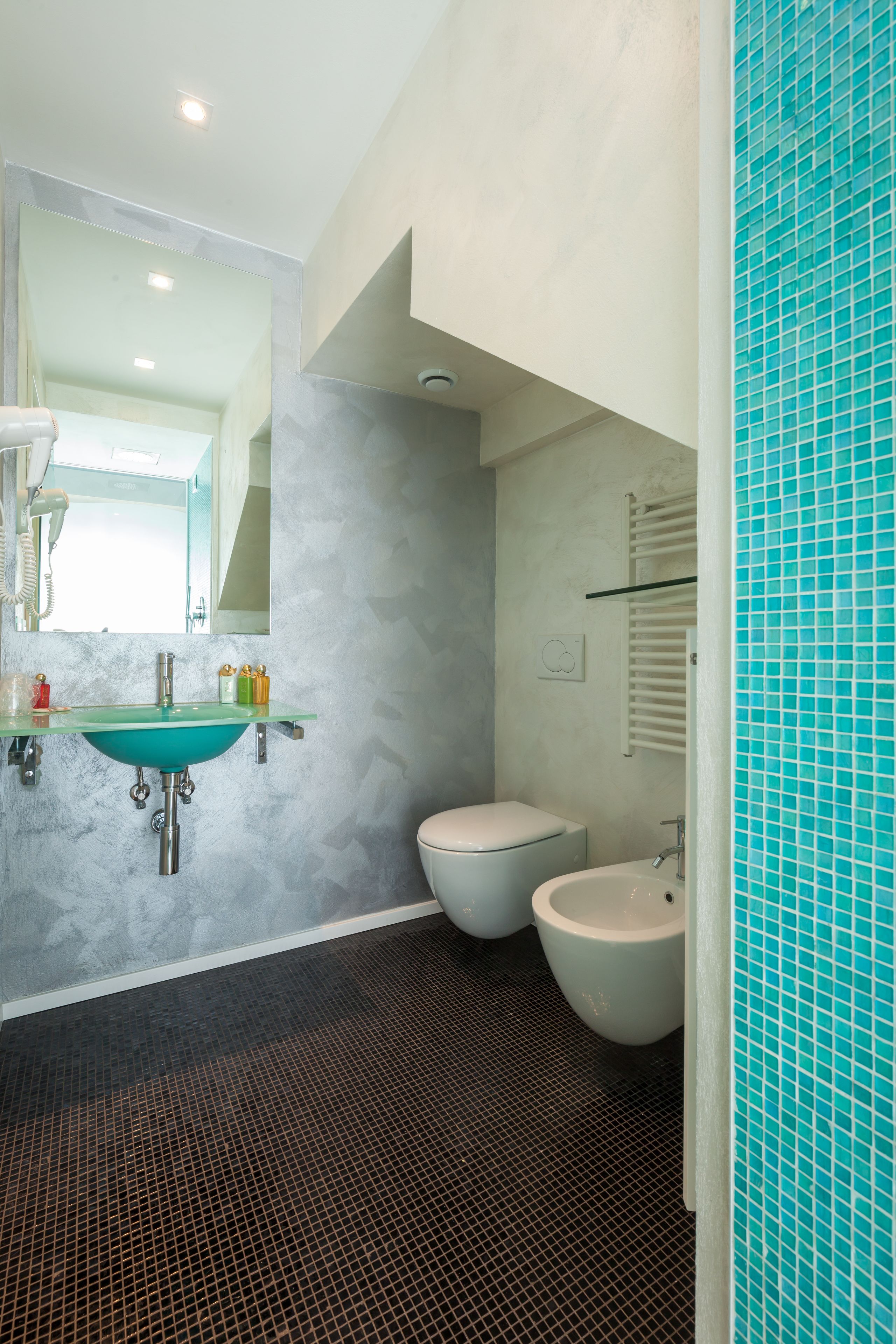 A modern bathroom with a glass sink, two toilets, and a tiled shower area.
