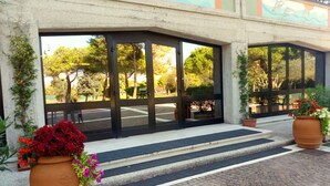 A building entrance with large glass doors, steps leading up to a door, and potted plants on either side. - Centro Vacanze Cavallino Opera Nascimbeni (Cavallino-Treporti)