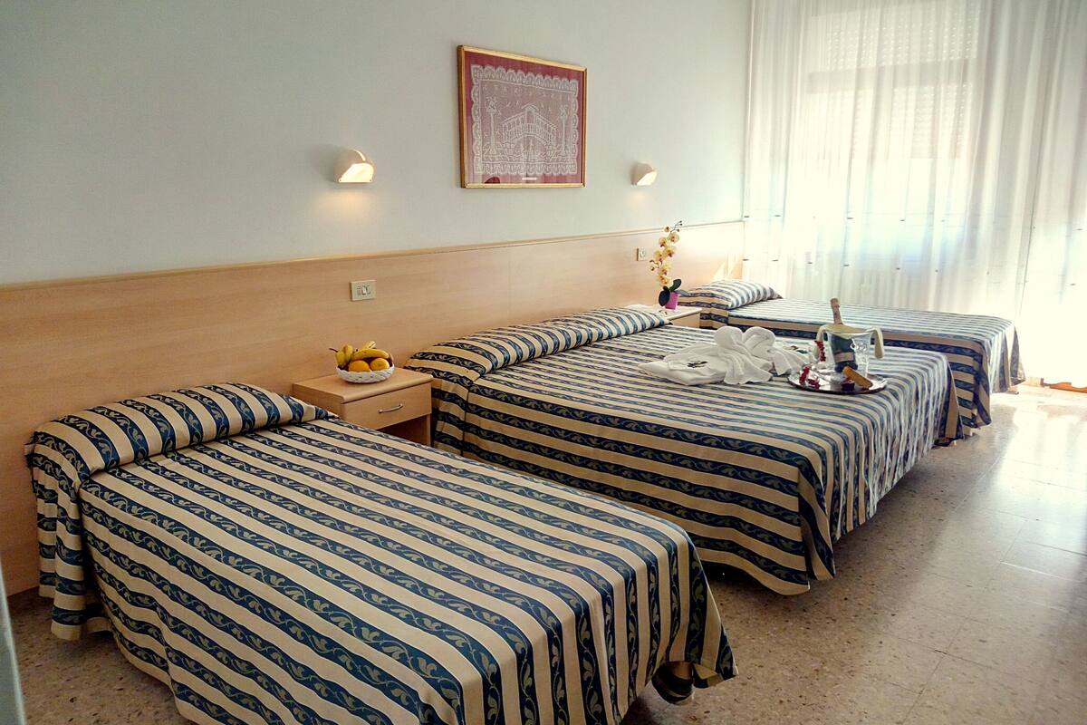 Ein Hotelzimmer mit zwei Betten, einem kleinen Tisch mit Früchten, einer Wandlampe und einem gerahmten Bild.