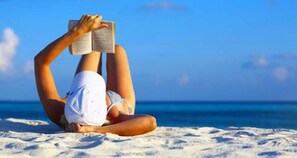 Une personne allongée sur une plage de sable, en train de lire un livre.