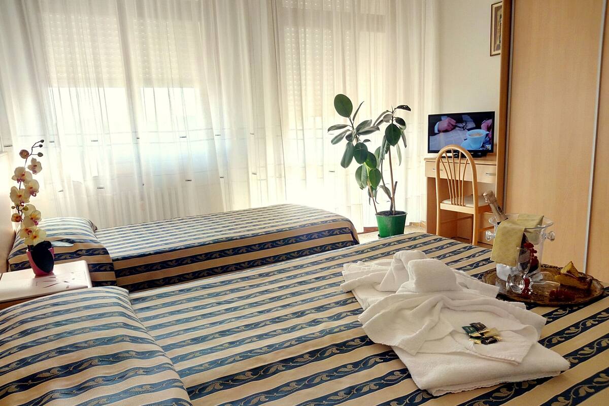 Ein Hotelzimmer mit zwei Betten, einem Fernseher, einer Pflanze und einem Tablett mit Getränken und Obst.