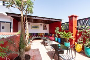 Patio esterno con parete rossa, una pergola in legno e diverse piante in vaso.