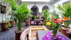 An indoor courtyard with potted plants, a small fountain, and a table with a purple tablecloth. - Ryad Amiran & Spa (Marrakech)