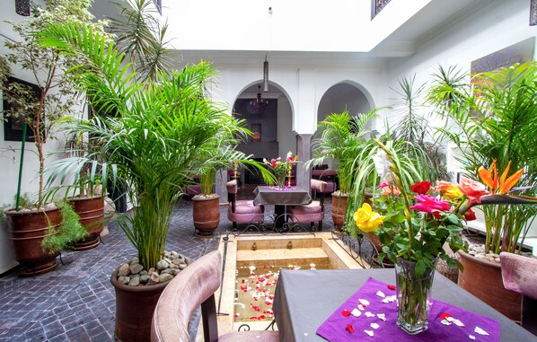 Un cortile interno con piante in vaso, una piccola fontana e un tavolo ricoperto da una tovaglia viola.