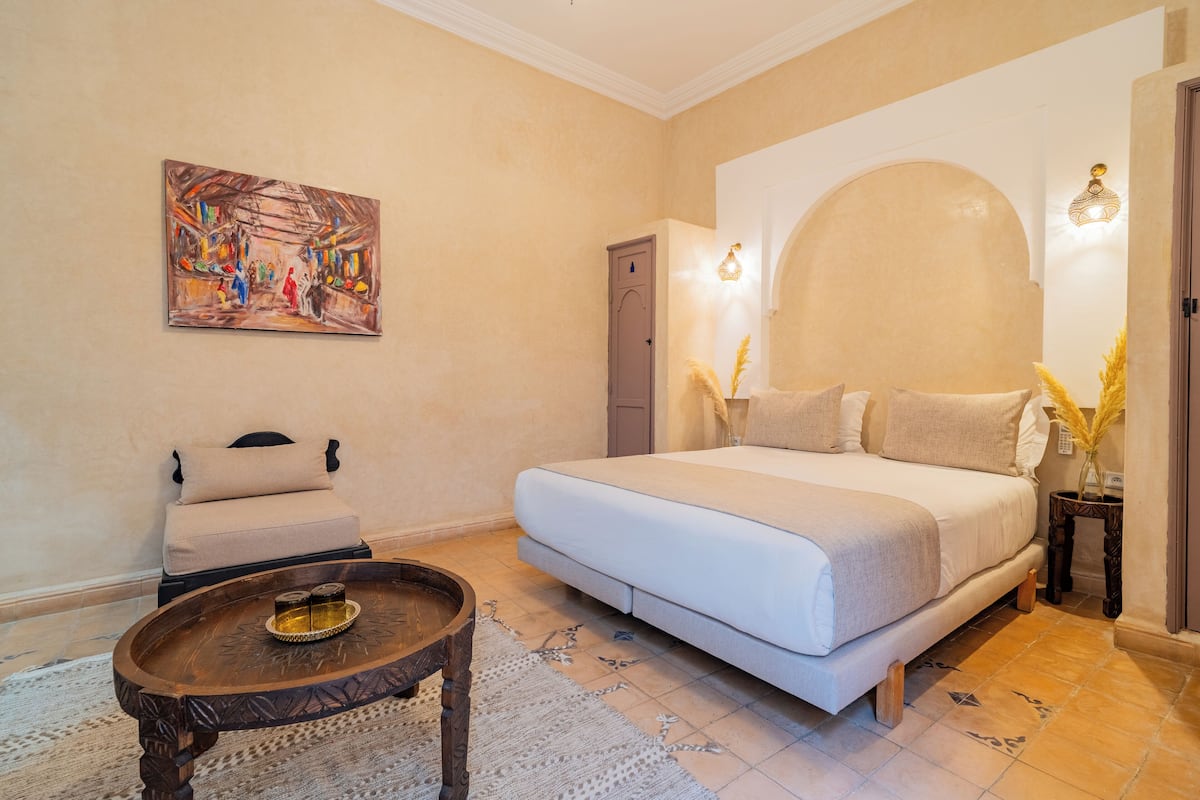 Un dormitorio con una cama, una mesita, una silla y un cuadro en la pared.