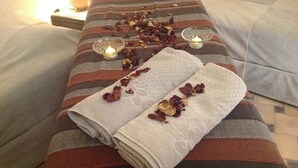 Una cama bien hecha con dos toallas dobladas y flores secas sobre un almohadón a rayas.