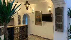 A lobby with a decorative metal counter, wall-mounted lights, framed artwork, and a tiled floor. - Riad Abaka by Ghali (Marrakech)