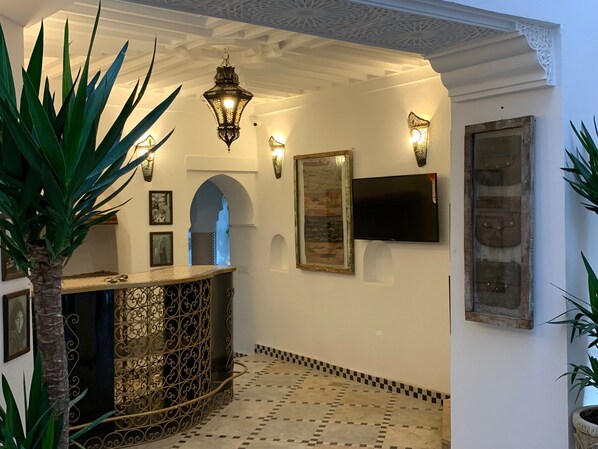 A lobby with a decorative metal counter, wall-mounted lights, framed artwork, and a tiled floor. - Riad Abaka by Ghali (Marrakech)