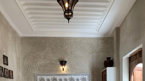 A bedroom with a large bed, two bedside tables with lamps, a decorative wall panel, and a wooden door. - Riad Abaka by Ghali (Marrakech)