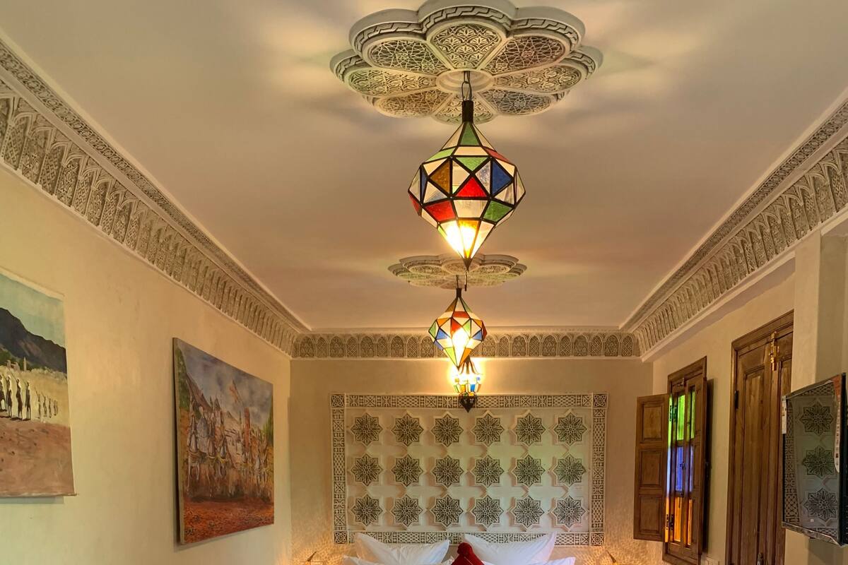 A room with a bed, two bedside tables, a red rug, and a decorative ceiling light.