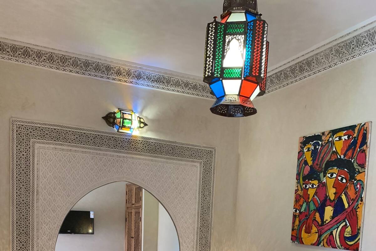 A bedroom with a red bedspread, a decorative mirror, a colorful painting, and a hanging lantern.