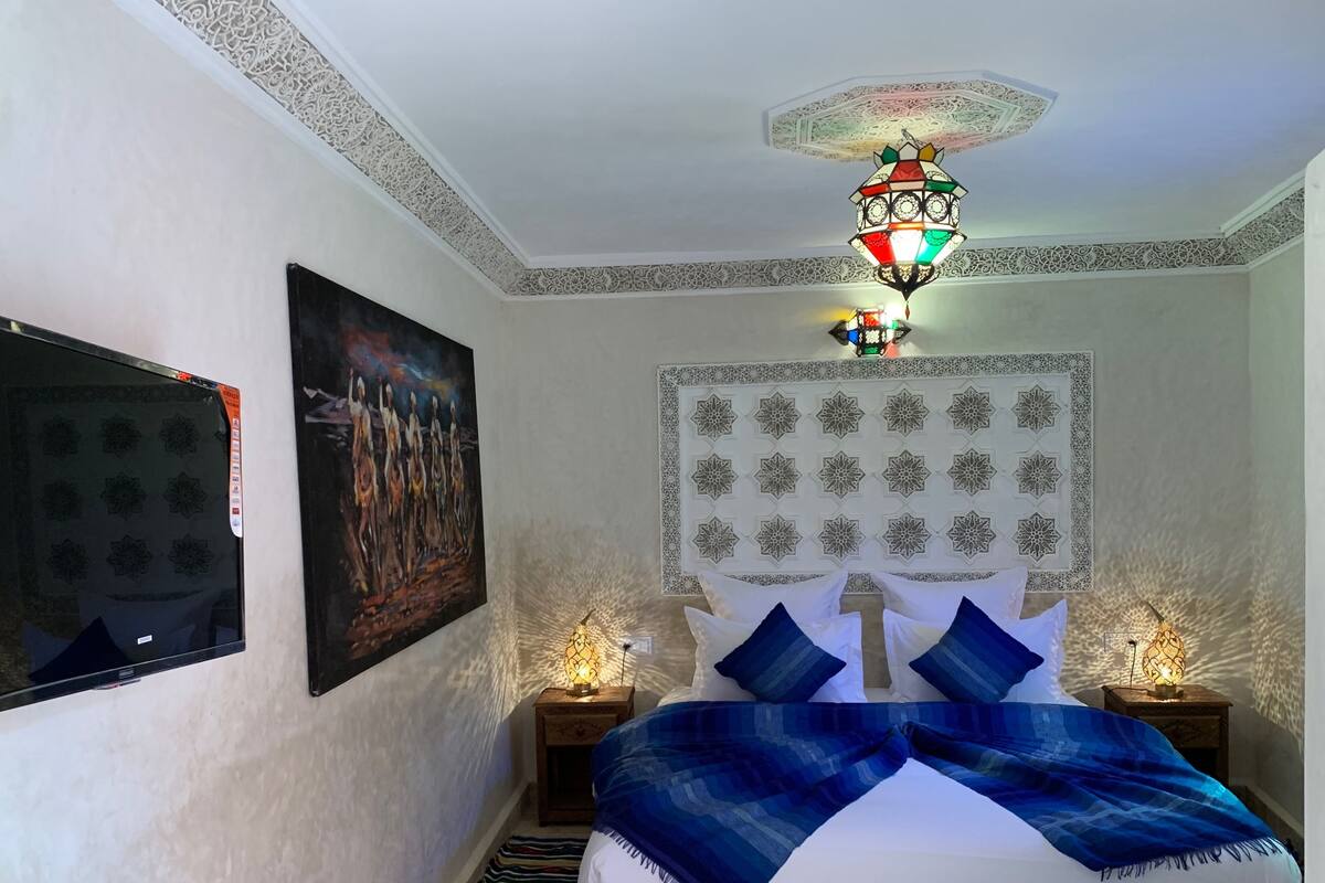 A bedroom with a bed, decorative wall panels, a painting, and a ceiling light fixture.