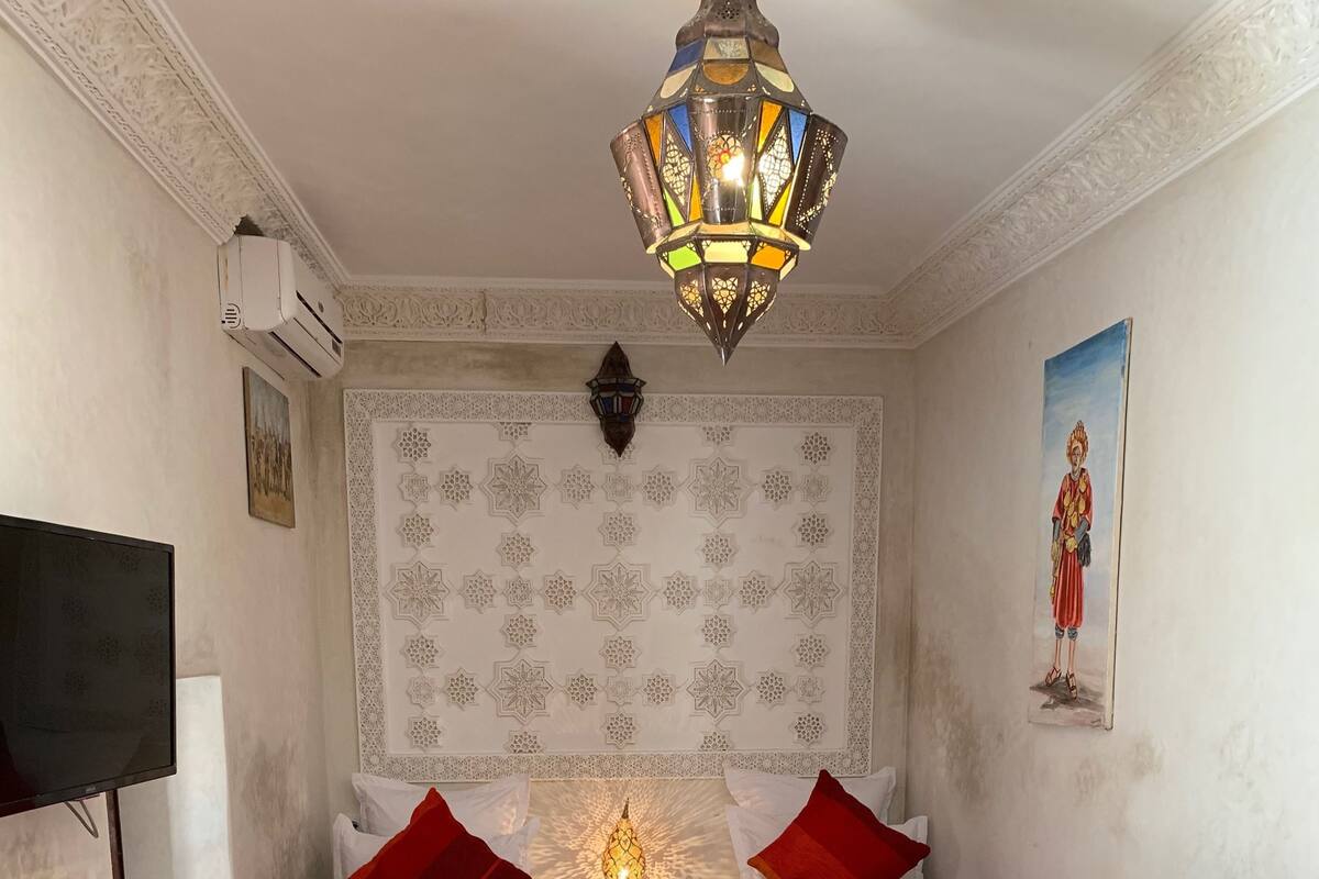 A hotel room with two beds, a TV, a decorative wall, and a ceiling light.