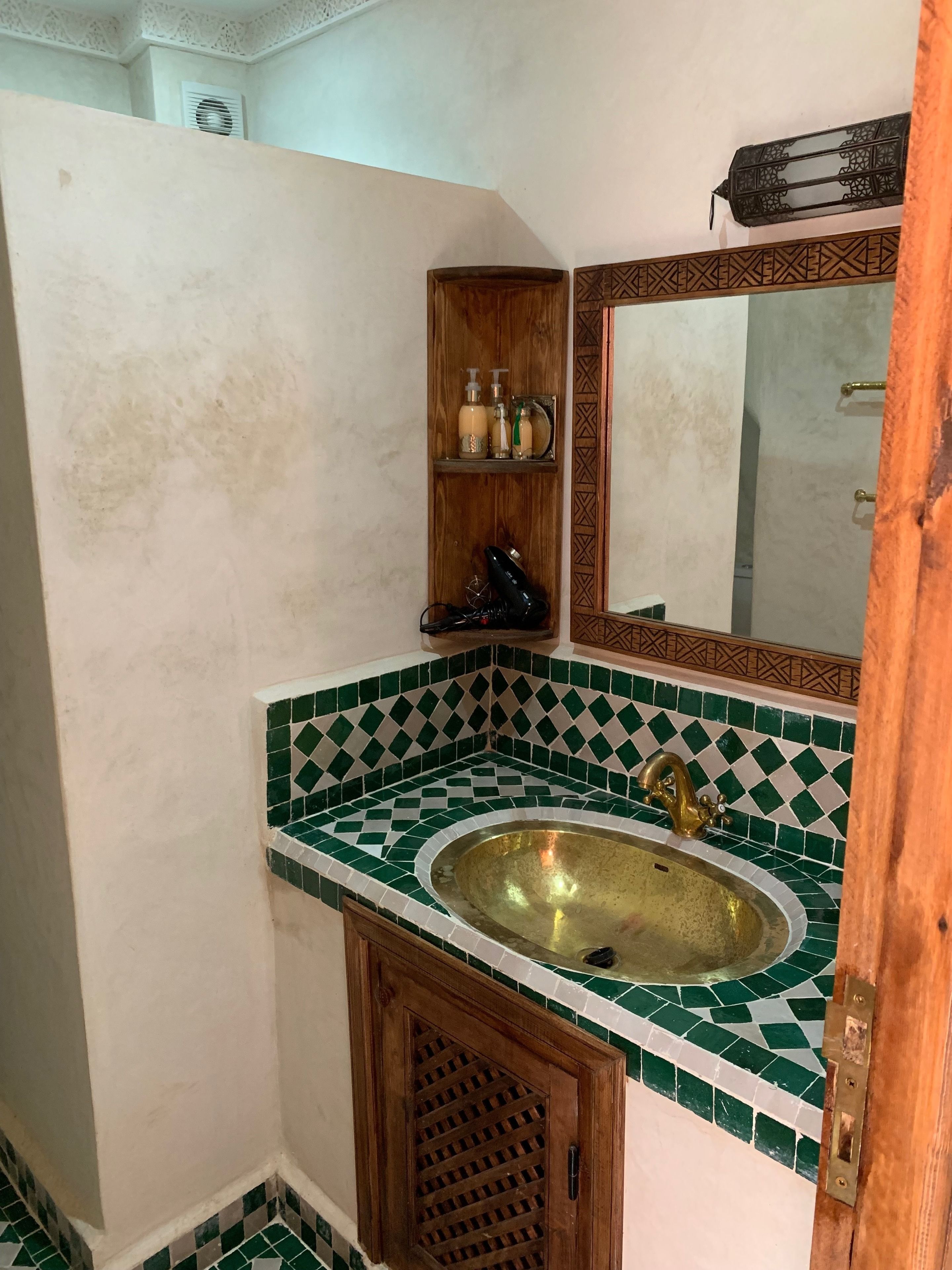 A bathroom with a green and white checkered tile backsplash, a brass sink, and a wooden cabinet above the sink.