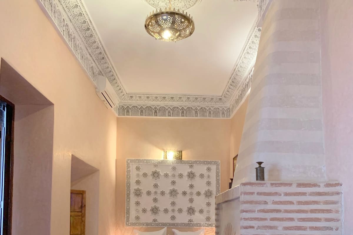 A cozy hotel room with a bed, a small table, a chair, and a decorative wall hanging.