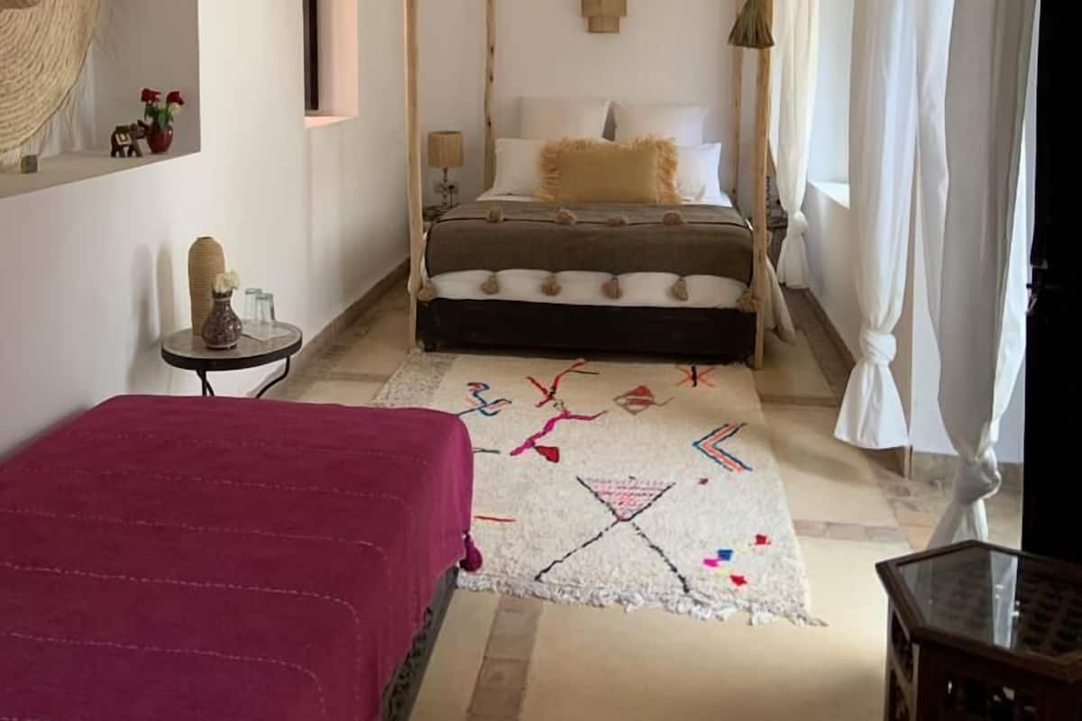 Un dormitorio con cama con dosel, lámpara colgante, espejo y una mesita con adornos.