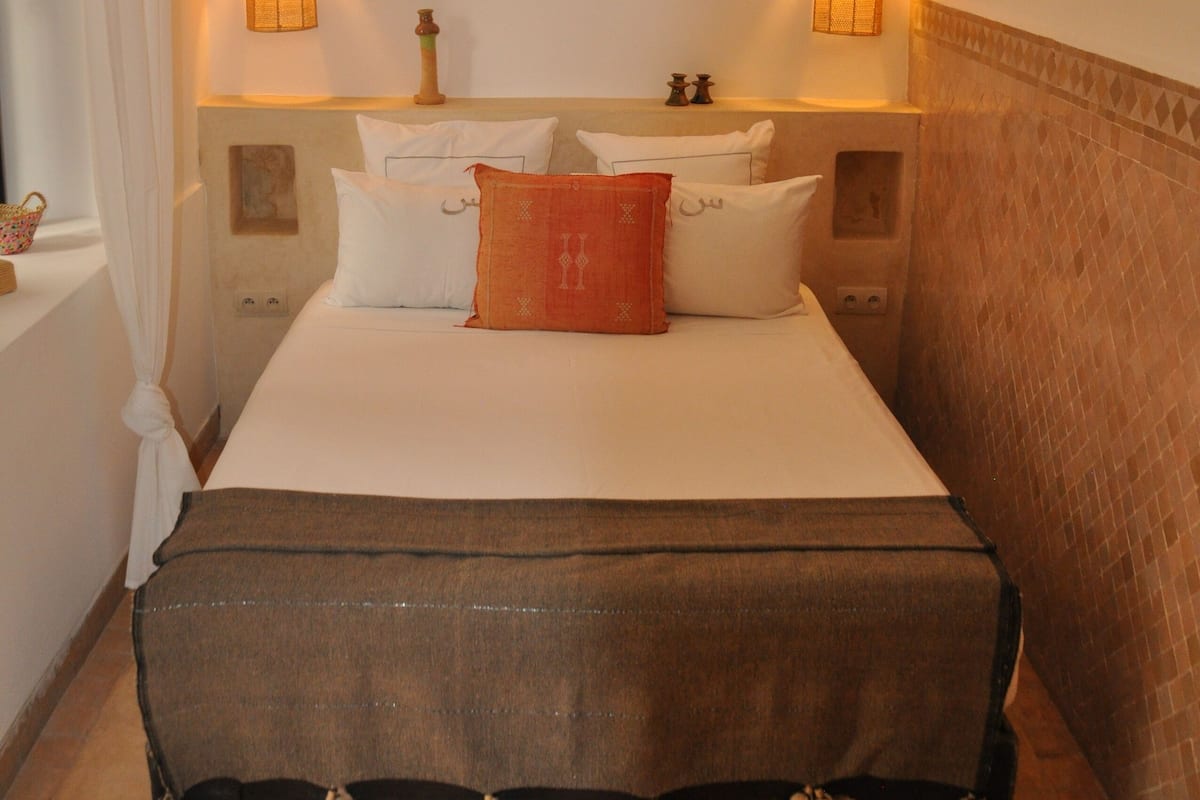 Habitación de hotel con una cama grande, dos lámparas de noche, una mesita de noche y una alfombra estampada.