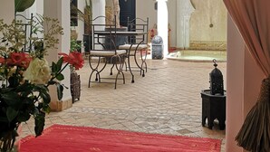 An indoor courtyard with a red carpet, a table with chairs, and a hanging plant. - Riad Sin (Marrakech)