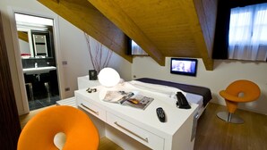 A modern bedroom with a wooden ceiling, a white bedside table, a bed, a TV, and an orange chair. - Hotel Coppe (Trieste)