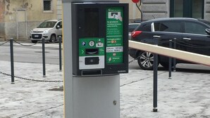 A parking meter with a green payment interface, located on a city sidewalk with a chain barrier. - Hotel Coppe (Trieste)