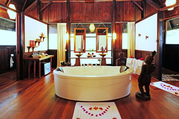 A large bathtub in a wooden room with a table and shelves.