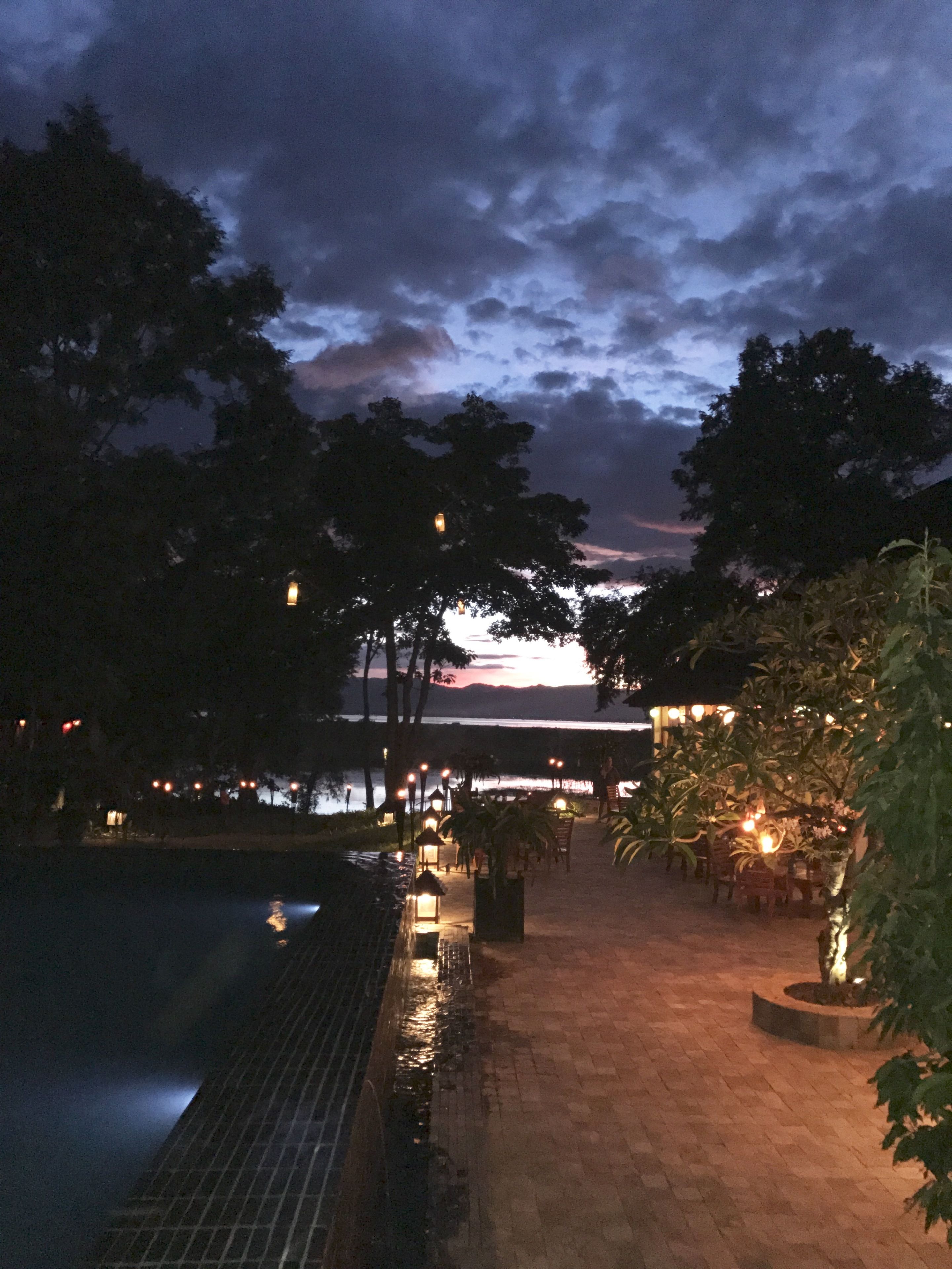 Un espacio al aire libre iluminado de noche con piscina, sendero y árboles.